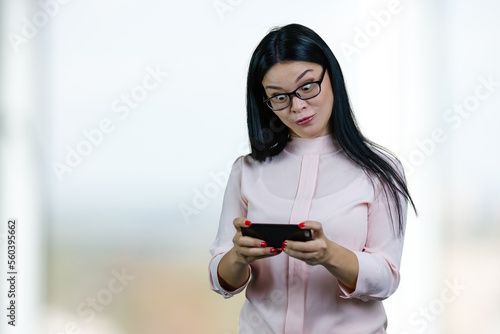 Asian businesswoman is watching something on her smartphone with eyes wide open. Abstract blurred background. photo