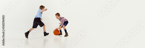 Two boys, children in classical retro clothes playing basketball over grey studio background. Banner, flyer. Concept of game, childhood, friendship