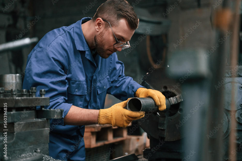 Busy by working with automatic machine. Man at factory and in blue uniform is indoors Busy by working with automatic machine. Man at factory and in blue uniform is indoors