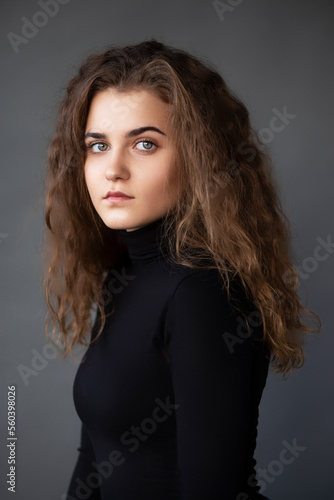 Front image portrait of a girl with curly hair, dressed in a black , on a grey background.