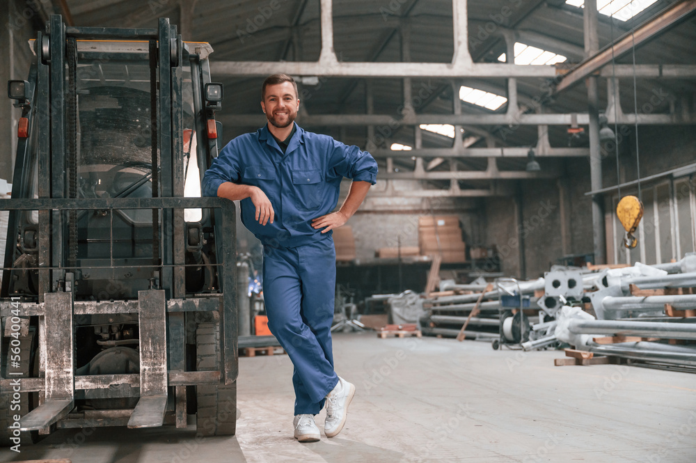 Fototapeta premium Leaning on the forklift. Factory worker in blue uniform is indoors