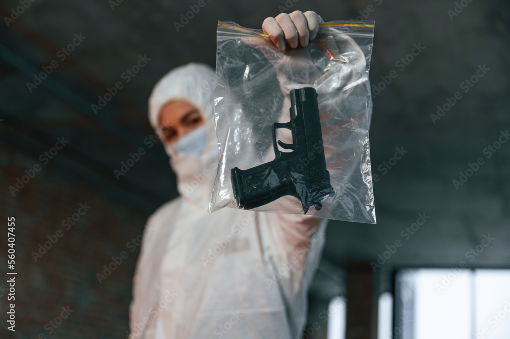 Obraz premium Woman in protective clothes is indoors holding pistol. Evidence of murder. Crime scene