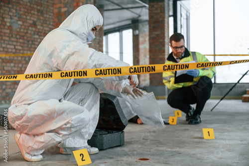 Woman holds the sleeve from the cartridge and puts it in the bag. Detectives are collecting evidence in a crime scene near dead body