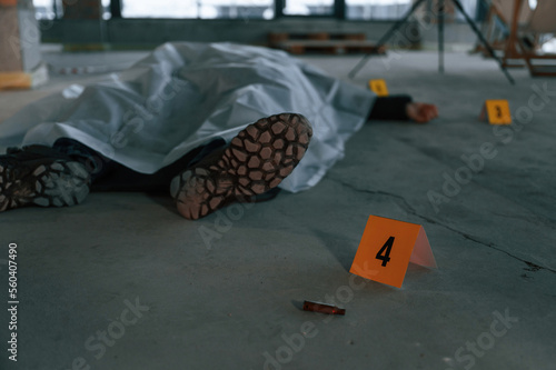 Bullet shell as clue. Dead body of a man is on the ground, covered in white cloth. Conception of murder, homicide