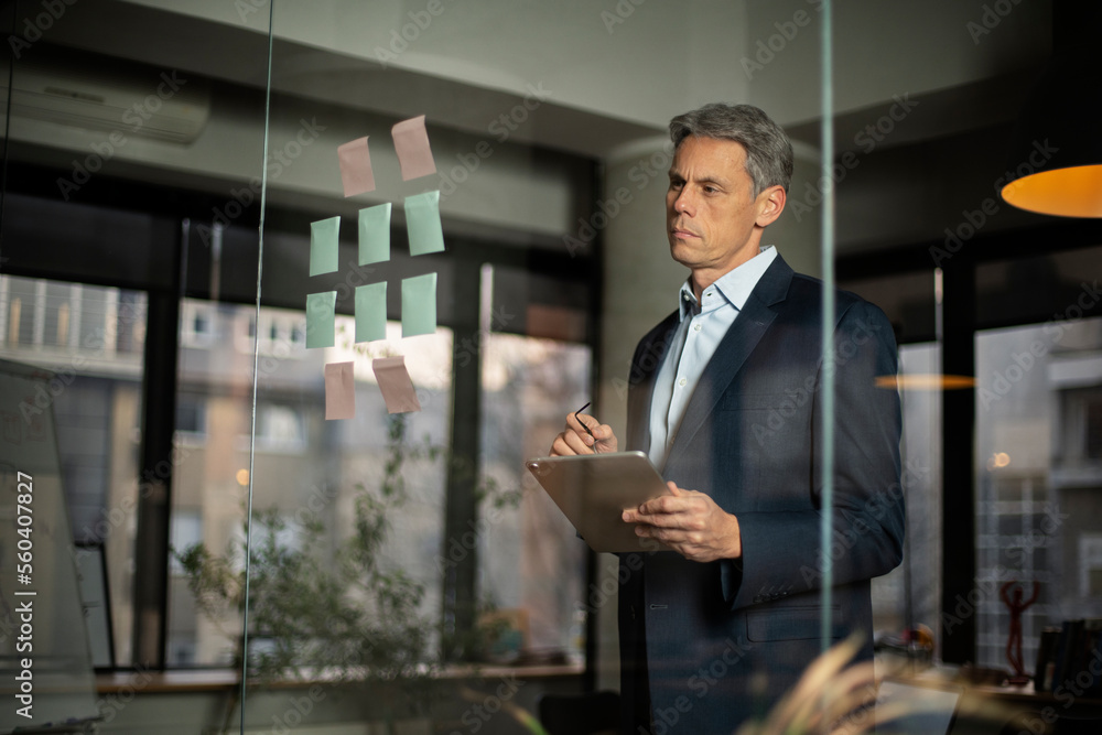 Portrait of successful businessman in office. Man writing ideas on colorful stickers on glass wall Portrait of successful businessman in office. Man writing ideas on colorful stickers on glass wall