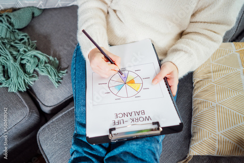 Top view close up young woman drawing work-life balance wheel sitting on the sofa at home. Self-reflection and life planning. Coaching tools. Finding Balance in Your Life. Selective focus photo