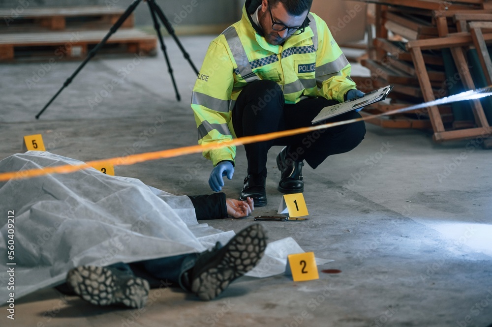 Knife is on the floor. Male detective is collecting evidence in a crime scene near dead body on the construction site Knife is on the floor. Male detective is collecting evidence in a crime scene near dead body on the construction site