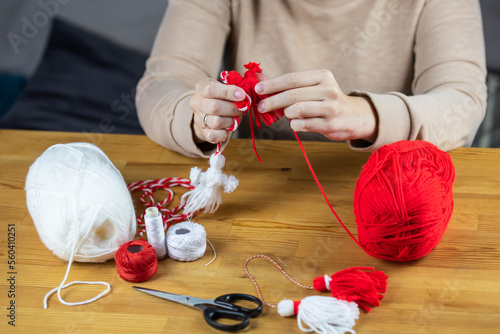 Woman making handmade traditional martisor, from red and white strings with tassel. Symbol of holiday 1 March, Martenitsa, Baba Marta, beginning of spring in Romania, Bulgaria, Moldova photo