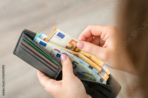 Woman holding her wallet with euro banknotes and counting them. Purchasing, buying goods, business and wealth concept