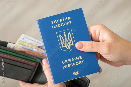 Ukrainian biometric passport in female hands, wallet with hryvnia money on the background. Travelling and working, wealth, money and finances concept
