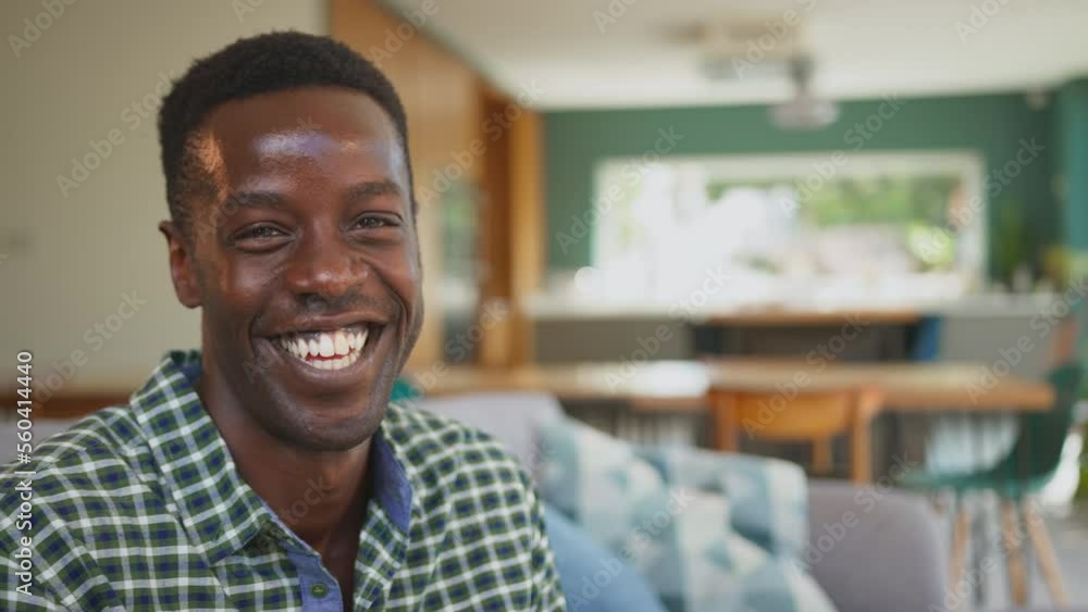 Portrait of man sitting on sofa in stylish lounge dining room smiling and laughing at camera - shot in slow motion Portrait of man sitting on sofa in stylish lounge dining room smiling and laughing at camera - shot in slow motion