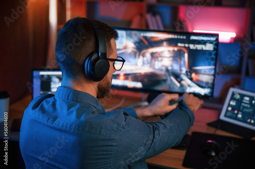 Concentrated man is playing the shooter game on his computer. Neon lighting