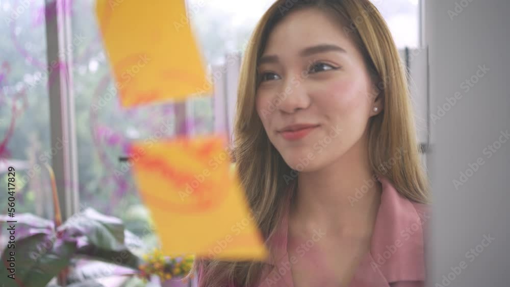 Young Creative businesswoman holding a marker and writing plan and share idea on glass wall with sticky note, Brainstorming and discussing and formulating, business strategies in tech startup office. Young Creative businesswoman holding a marker and writing plan and share idea on glass wall with sticky note, Brainstorming and discussing and formulating, business strategies in tech startup office.