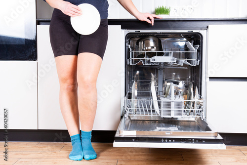Obraz na płótnie Woman is showing the clean plate with dishwasher in dirty kitchen, cropped image. Opened dishwasher with clean dishes. w salonie
