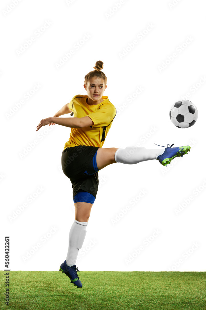 Concentrated young woman, professional female football player in motion, training, playing football, soccer isolated over white background