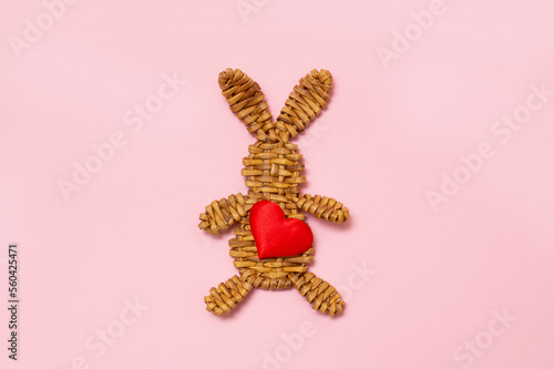 wicker bunny with a heart in his hands on a pink background. Love. Valentine's Day.