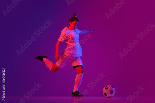 Young professional female football, soccer player in motion, training, playing over gradient pink background in neon light. Making goal