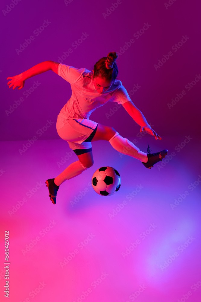 Dribbling. Young professional female football, soccer player in motion, training, playing over gradient pink background in neon light