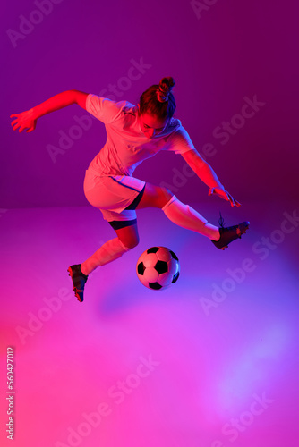 Dribbling. Young professional female football  soccer player in motion  training  playing over gradient pink background in neon light