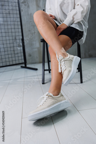 Female slender legs in beige casual sneakers with laces. Women's stylish leather summer shoes