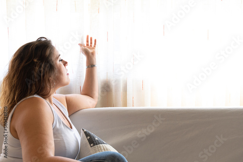 Profile view of a voluptuous woman sitting on a sofa looking through the curtains photo