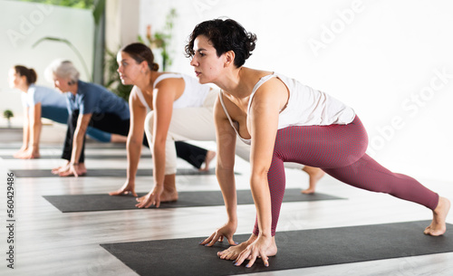 Active young Latin female in sportswear practicing various yoga positions during group training indoor