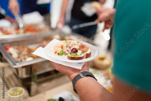 Close up of man holding plastic plate and scooping food at buffet table catering in hotel or restaurant