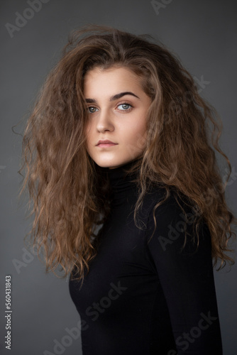 Front image portrait of a girl with curly brown hair, dressed in a black , on a grey background.
