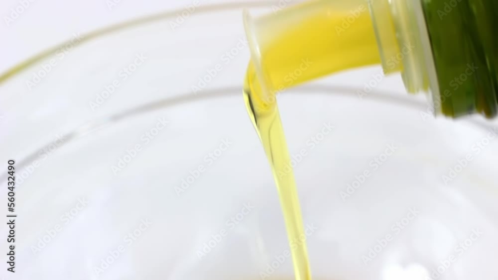 Yellow organic olive oil pouring from the bottle with dispenser into the bowl close up Yellow organic olive oil pouring from the bottle with dispenser into the bowl close up