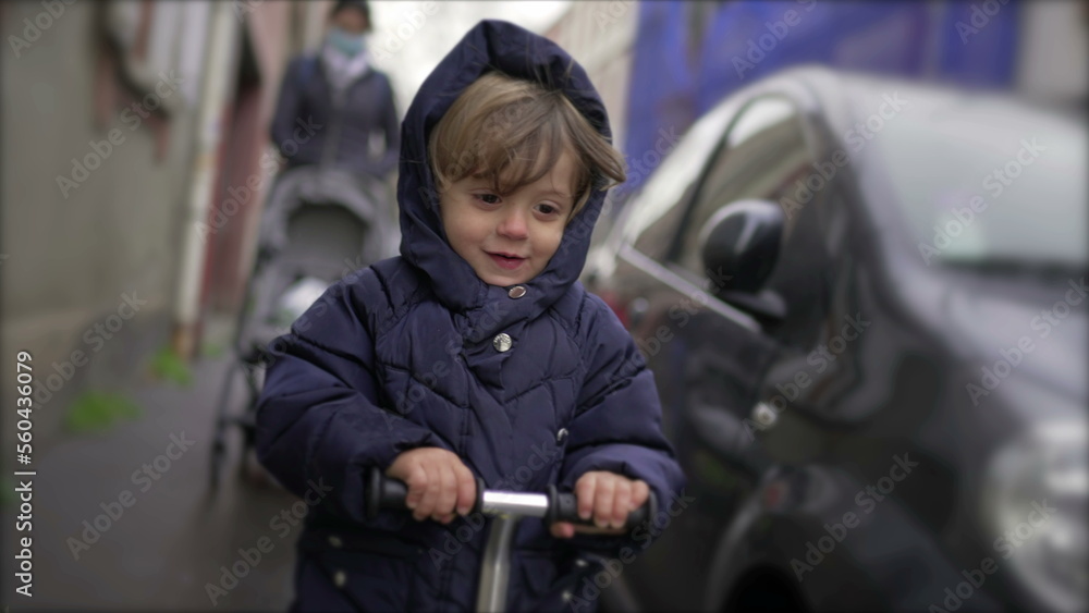 Happy toddler boy riding scooter outside on sidewalk, active child rides scooter Happy toddler boy riding scooter outside on sidewalk, active child rides scooter