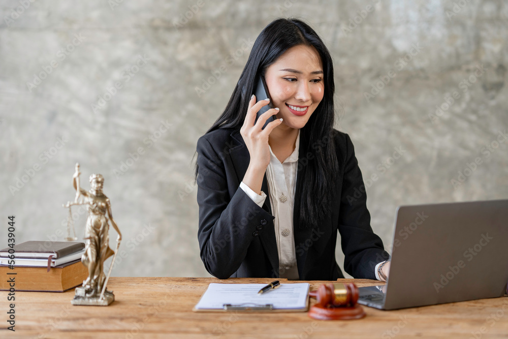 Beautiful young woman lawyer or legal advisor talking on the phone about contract papers with brass scales on wooden table in law office legal services advice justice. Beautiful young woman lawyer or legal advisor talking on the phone about contract papers with brass scales on wooden table in law office legal services advice justice.