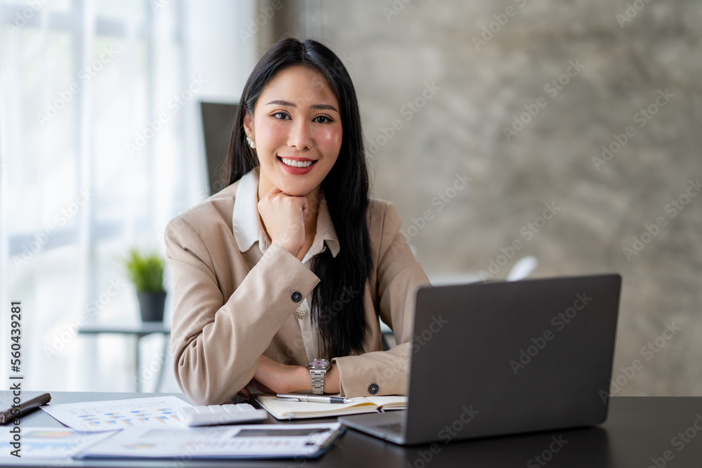 Asian young woman businesswoman using a laptop sitting smiling using modern analytical concepts While happily working at the desk in the office. Asian young woman businesswoman using a laptop sitting smiling using modern analytical concepts While happily working at the desk in the office.