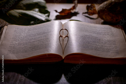 An old open book with a gold ring dropping a shadow in a form of a heart