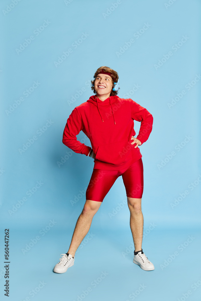 Workout. Young happy cheerful man in sportswear posing isolated over blue background. Concept of active healthy lifestyle, positive emotions, sport, fitness, ad