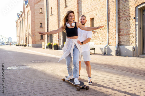 Couple having fun while driving a long board. Guy learning a girl skating. 