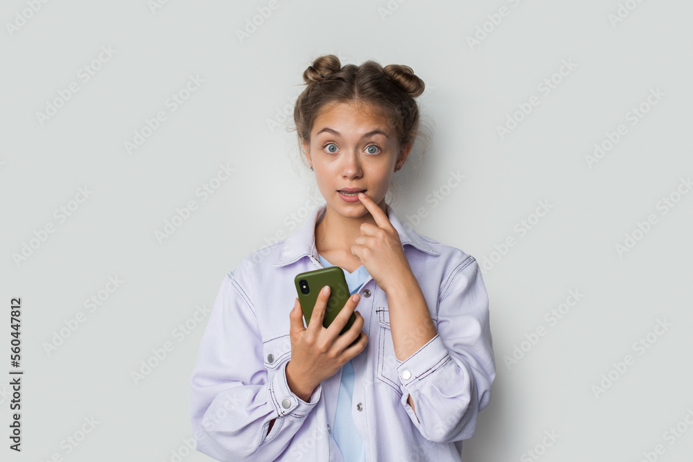 Photo of thoughtful young brunette woman wearing eyeglasses using mobile phone writing message isolated on white background.
