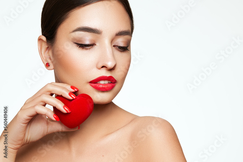 Young beautiful woman with heart-shaped gift. Girl with pure perfect face skin. Cosmetology  beauty and spa. Red nails manicure. Valentine   s Day