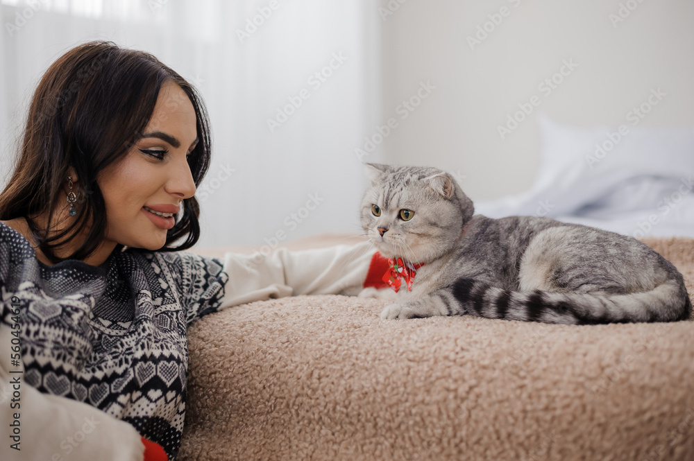 Beautiful young woman lies with a gray cat on the bed