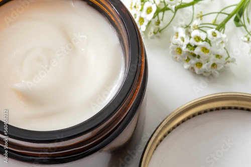 Face cream jar with open lid and white flowers