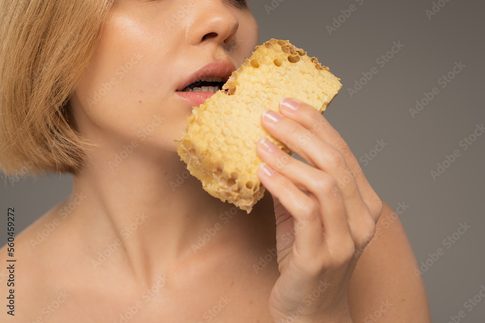 cropped view of young woman holding piece of sweet honeycomb near mouth isolated on grey. cropped view of young woman holding piece of sweet honeycomb near mouth isolated on grey.