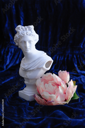 apollo sculpture next to a pink flower on a blue velvet background