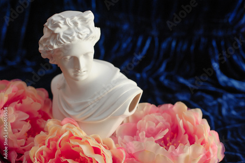 Greek sculpture among pink peonies on a blue velvet background. close up. copy space