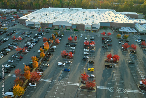 Aerial view of large parking lot in front of rgocery store with many parked colorful cars. Carpark at supercenter shopping mall with lines and markings for vehicle places and directions