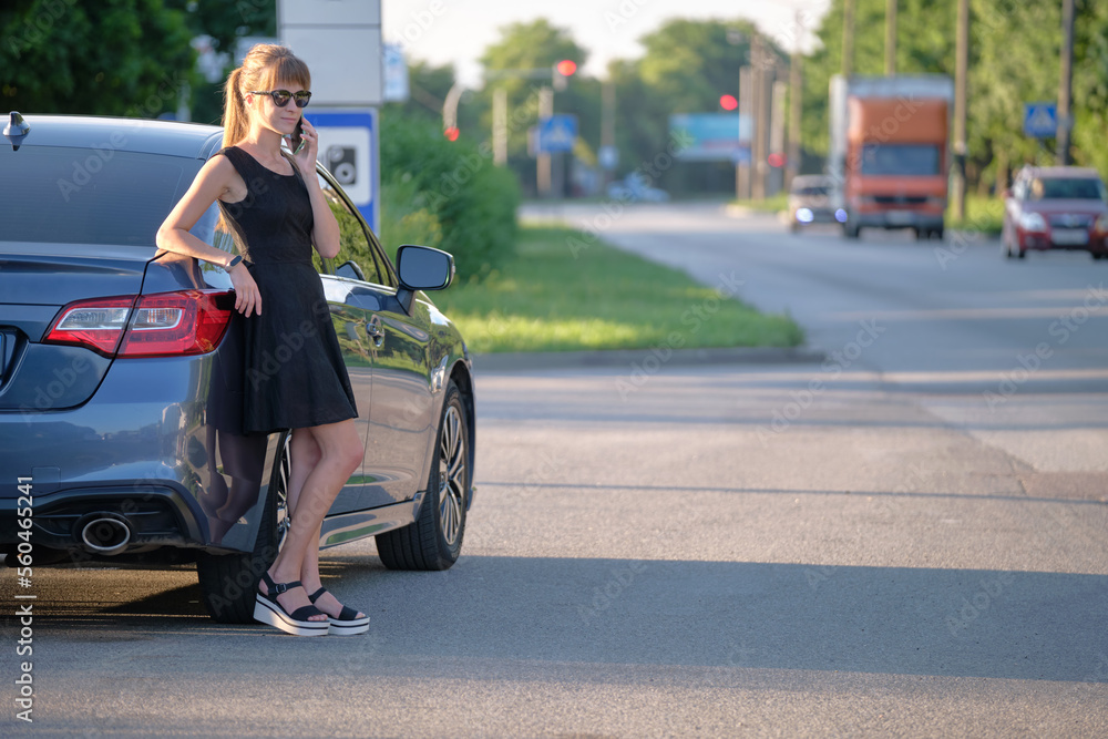 Young female driver standing near her car talking on mobile phone on a city street in summer Young female driver standing near her car talking on mobile phone on a city street in summer