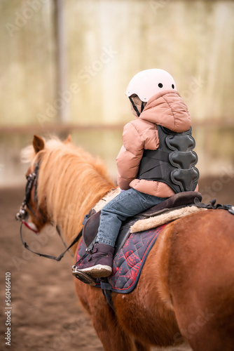 Little Child Riding Lesson. Three-year-old girl rides a pony and does exercises