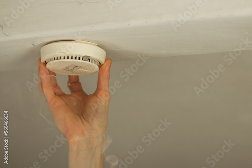 Male hand changing the battery and fixing the smoke alarm on ceiling of a home. Home or office safety concept. 