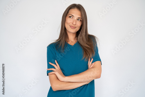 Portrait of charming young woman with crossed arms. Female Caucasian model with brown hair and grey eyes in turquoise T-shirt and casual blue jeans smiling looking away. Advertising, lifestyle concept