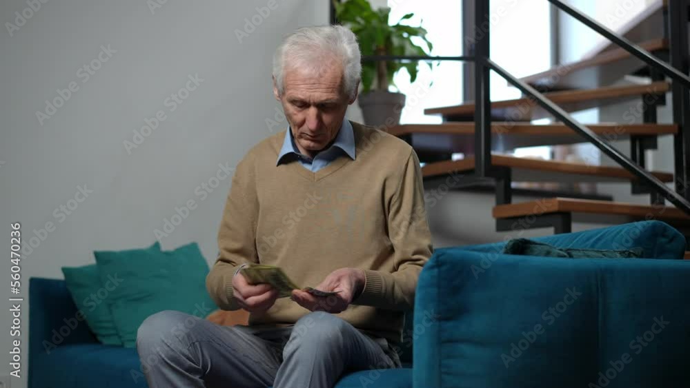 Sad lonely senior man counting cash looking away thinking sitting on couch in living room. Portrait of poor Caucasian male retiree planning budget calculating money at home Sad lonely senior man counting cash looking away thinking sitting on couch in living room. Portrait of poor Caucasian male retiree planning budget calculating money at home