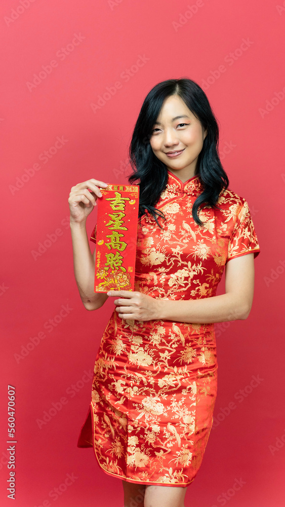 Beautiful woman wearing traditional cheongsam qipao dress holding blessing fortune card isolated on red background. Chinese text means great luck great profit Beautiful woman wearing traditional cheongsam qipao dress holding blessing fortune card isolated on red background. Chinese text means great luck great profit