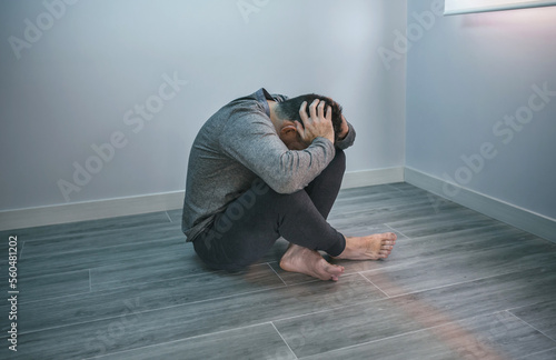 Unrecognizable man with problems holding his head with hands sitting on the floor